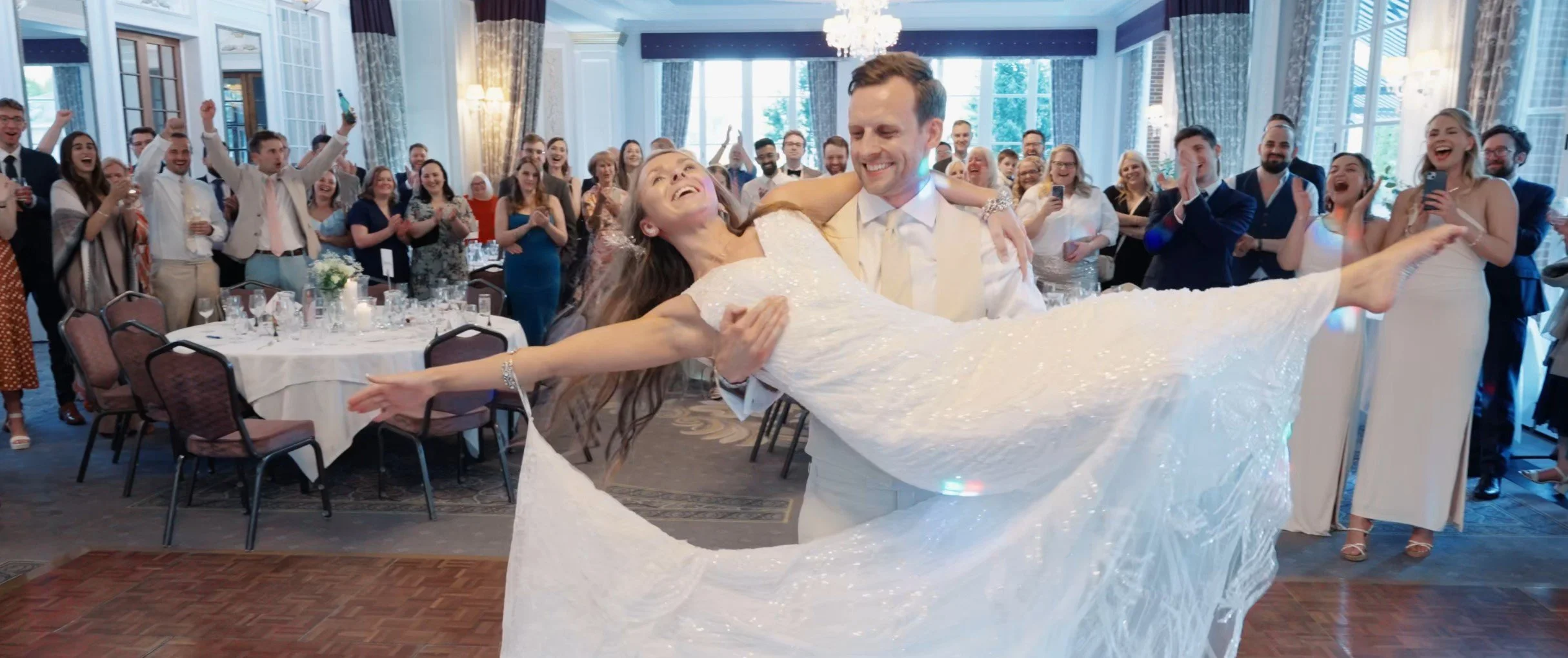 A wedding celebration with a bride and groom dancing, surrounded by cheering guests in a decorated banquet hall.