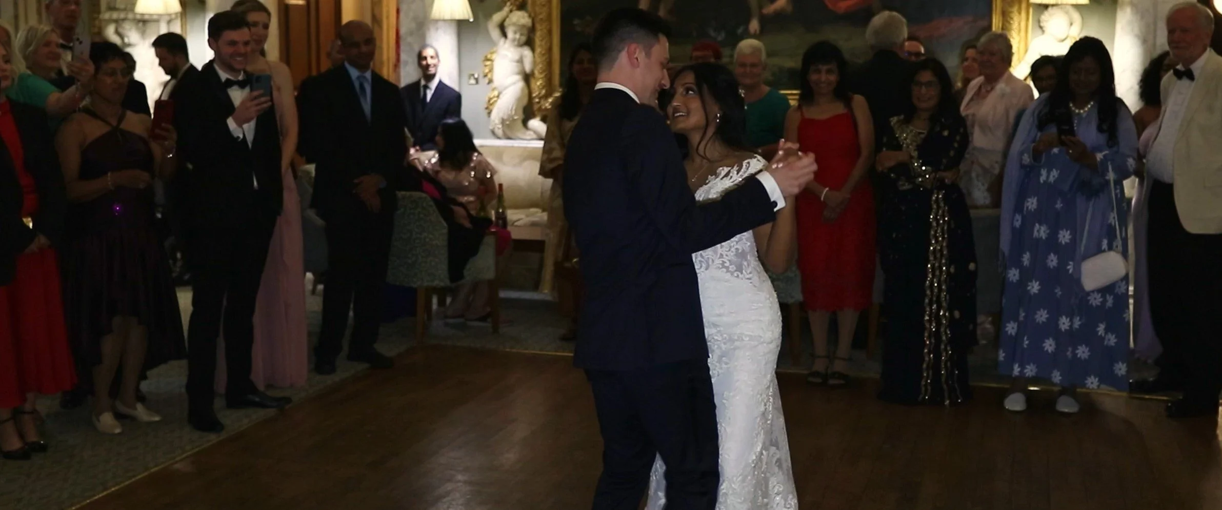 Couple dancing in front of guests at a wedding reception in an elegant room.