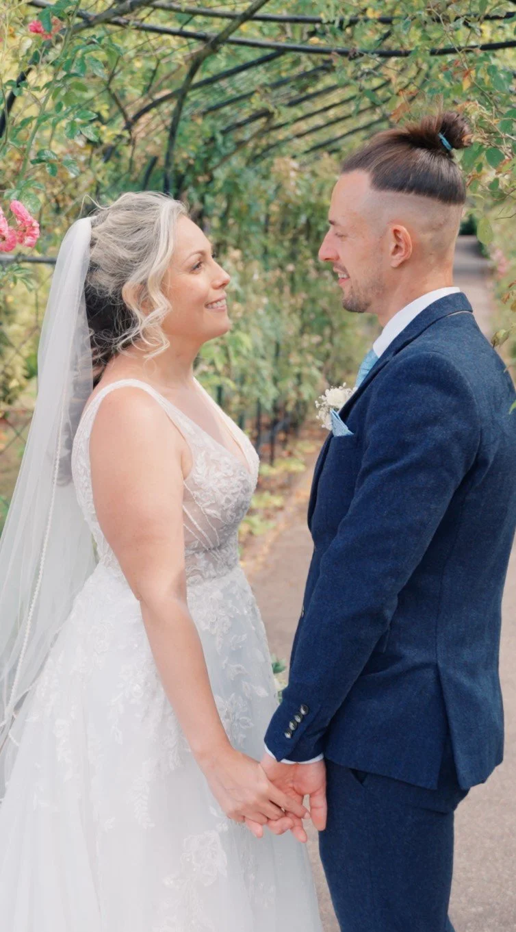 Bride and groom holding hands and smiling at each other outdoors during their wedding day.