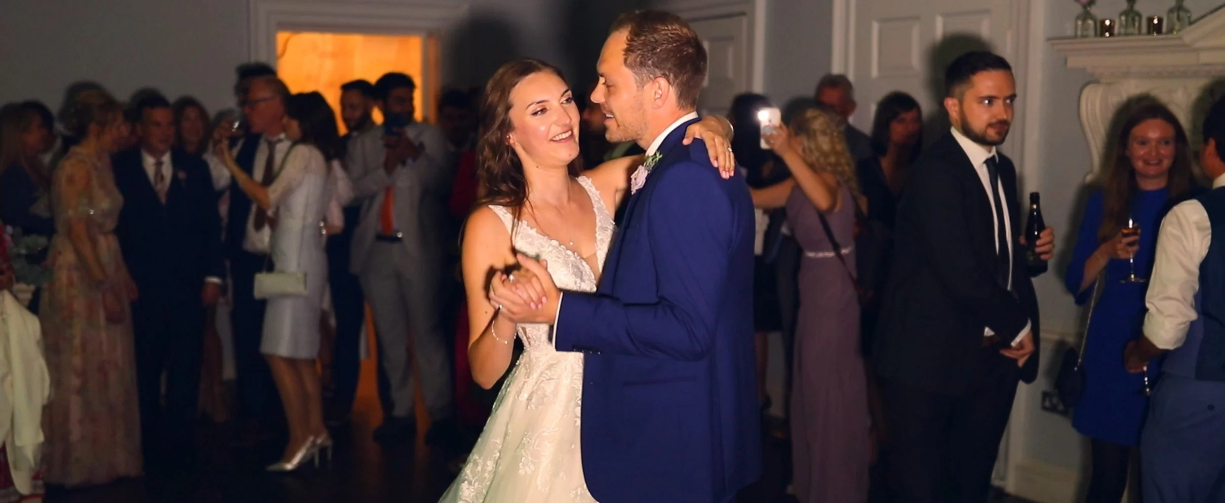 A bride and groom dancing at their wedding reception, surrounded by guests celebrating.
