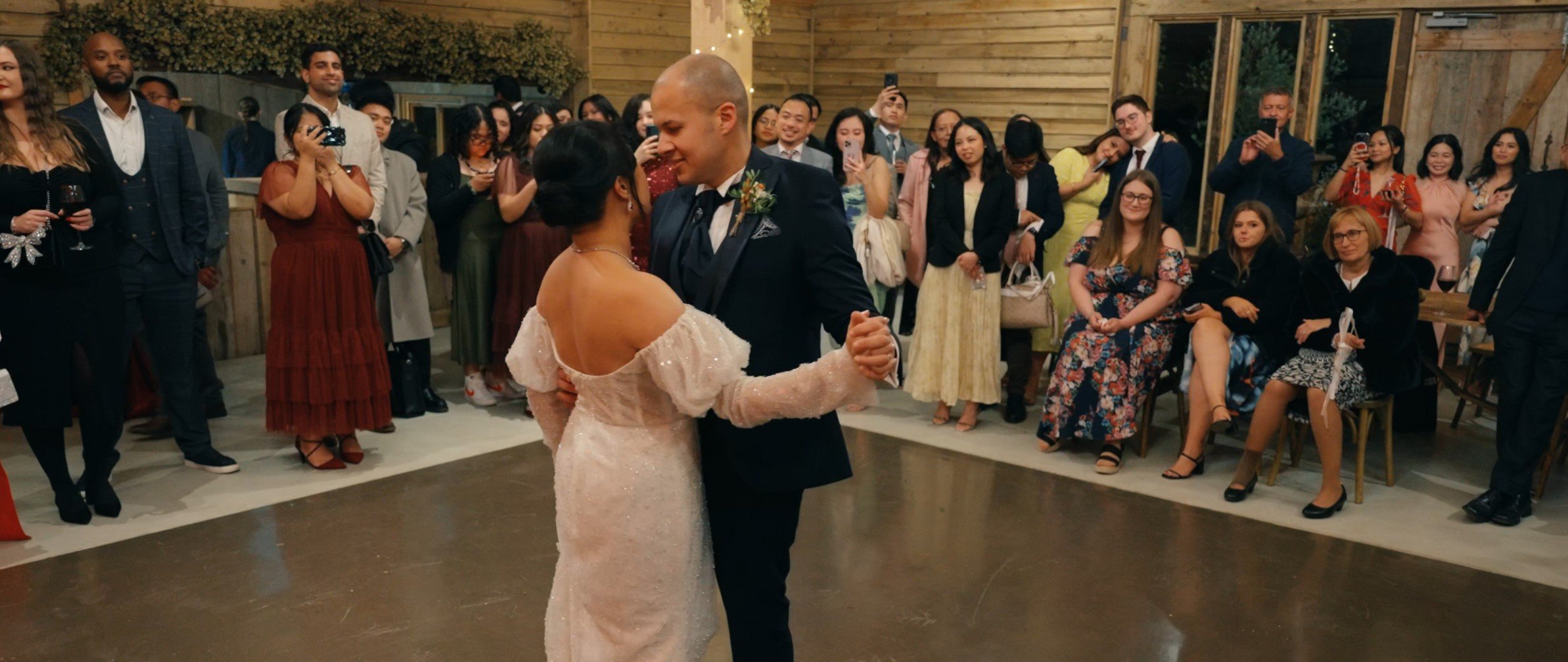 A bride and groom dancing at their wedding reception with guests watching and taking photos.