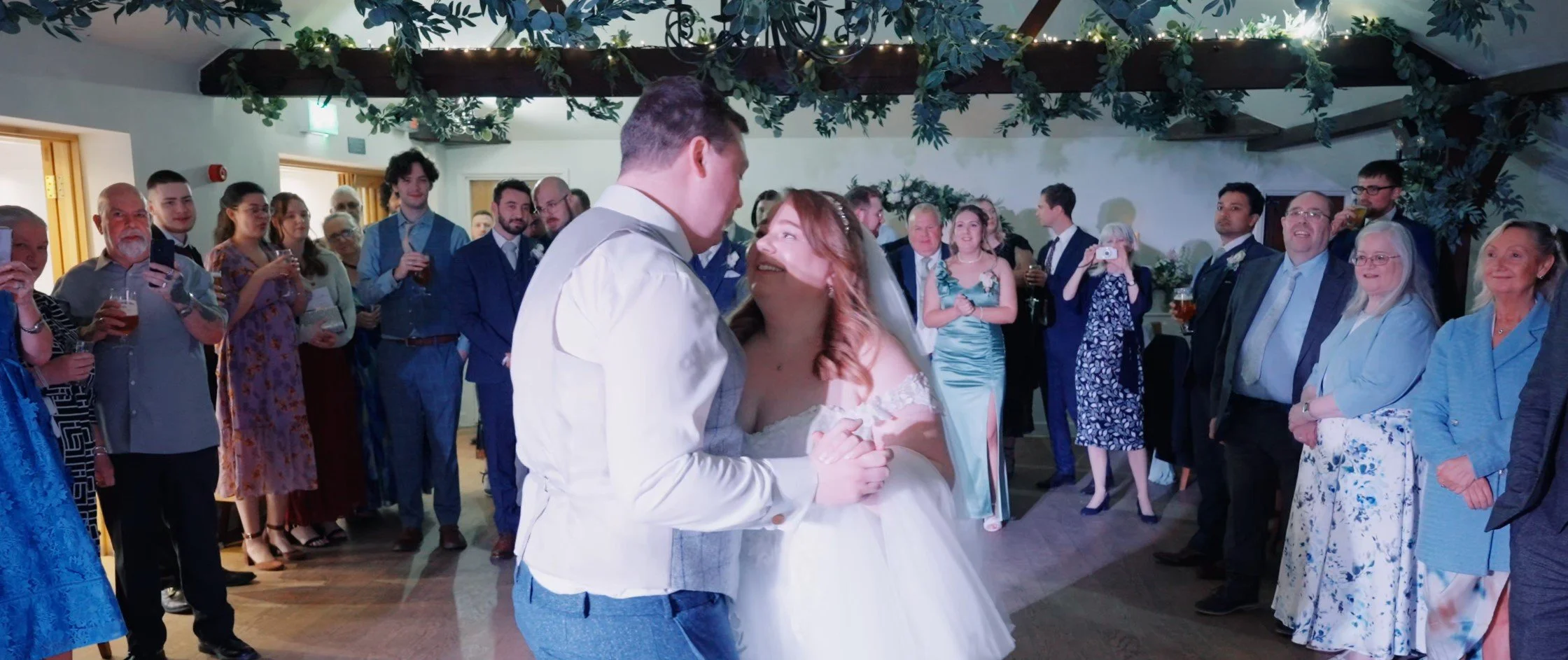 A bride and groom dance at their wedding reception as guests watch and take photos.