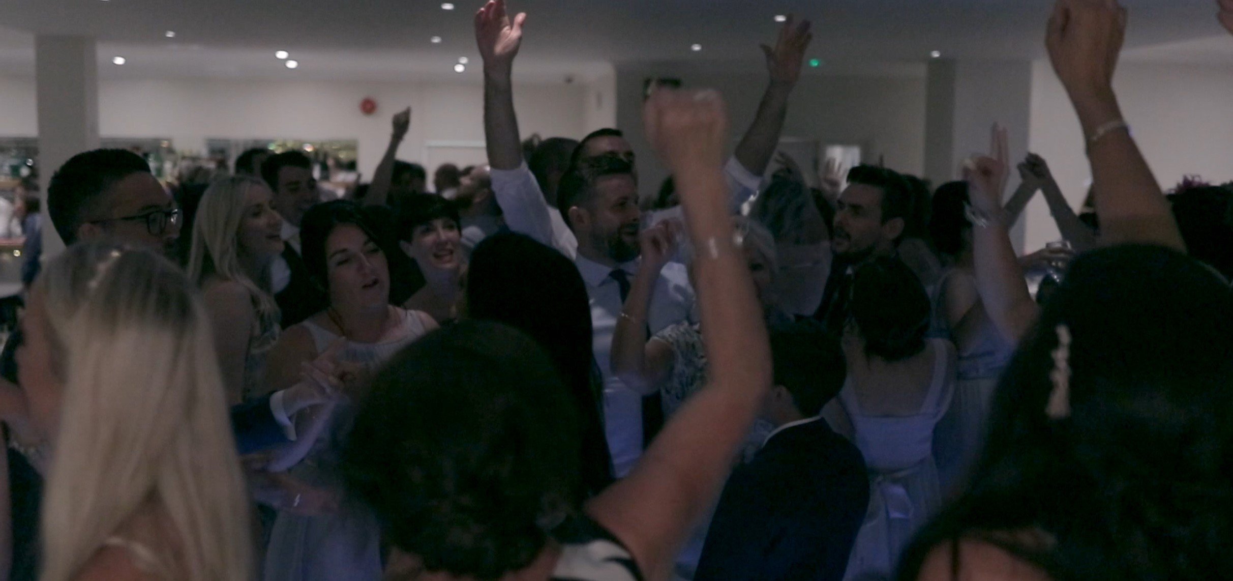 Group of people celebrating, some with hands raised, in a dimly lit event hall.