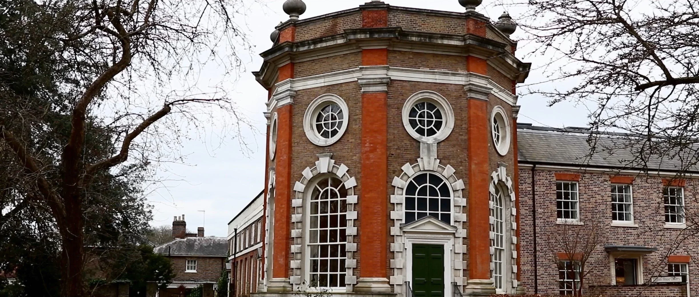 Historical brick building with ornate windows and a green door, surrounded by leafless trees.