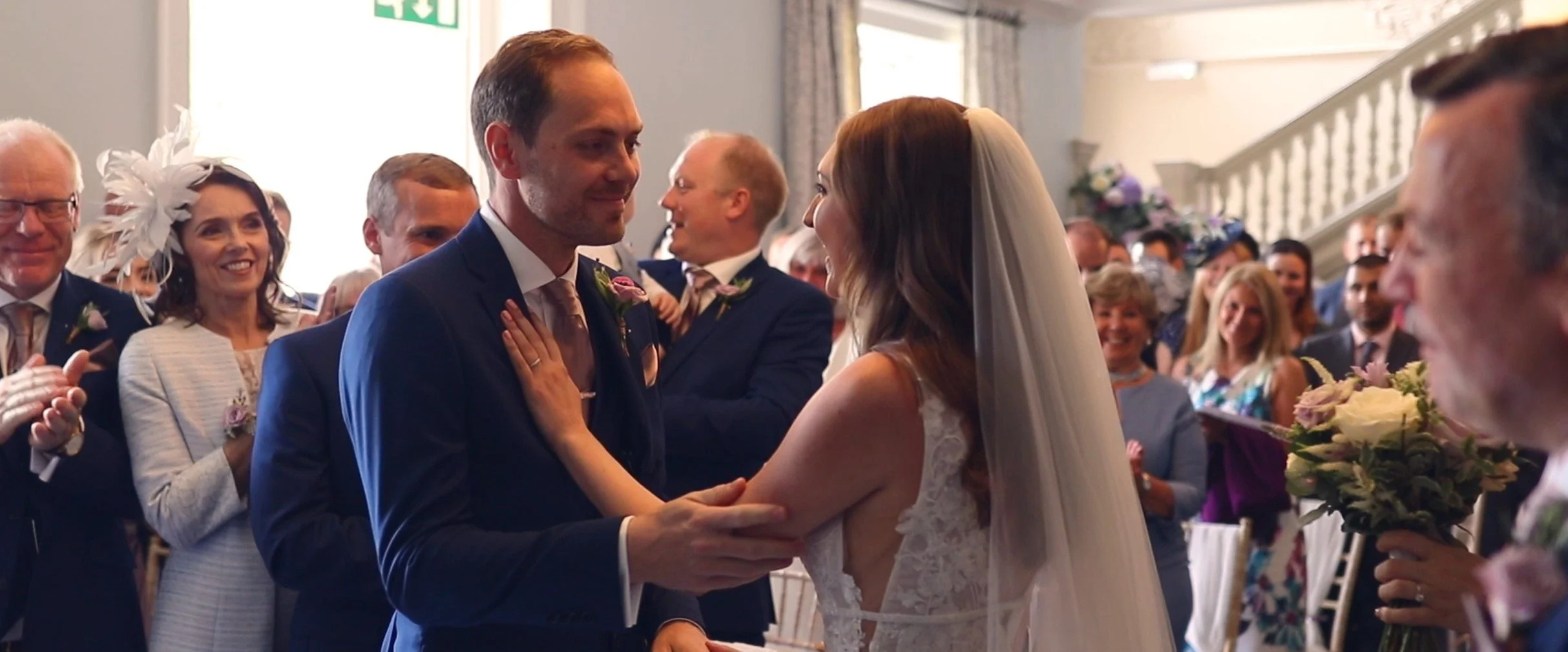 A bride and groom exchanging vows at their wedding ceremony with guests smiling and clapping