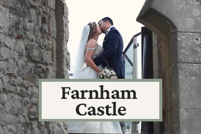 A bride and groom kissing at Farnham Castle during their wedding, with stone walls and castle architecture in the background.