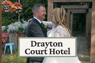 A newlywed couple in wedding attire smiling and embracing outdoors at the Drayton Court Hotel.