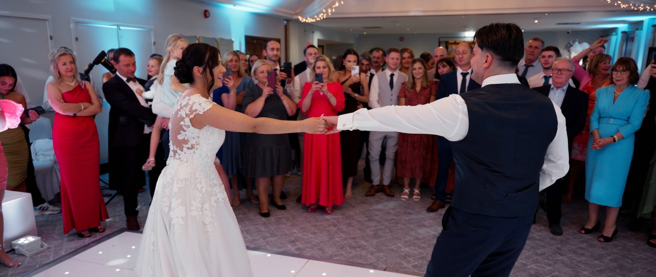 Bride and groom dancing at their wedding reception surrounded by guests watching and taking photos.