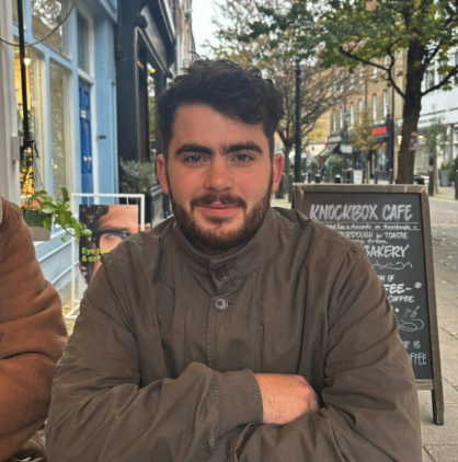 Man zit buiten bij een café op een straat in de herfst, met een zwartbord met menukaart op de achtergrond.