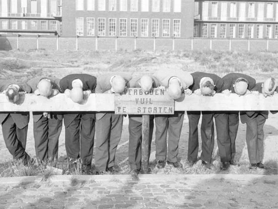 Zeven mensen met hoofden op een tafel, met een bord tussen hen dat zegt 'Verbergen jullie uw stoerten'.