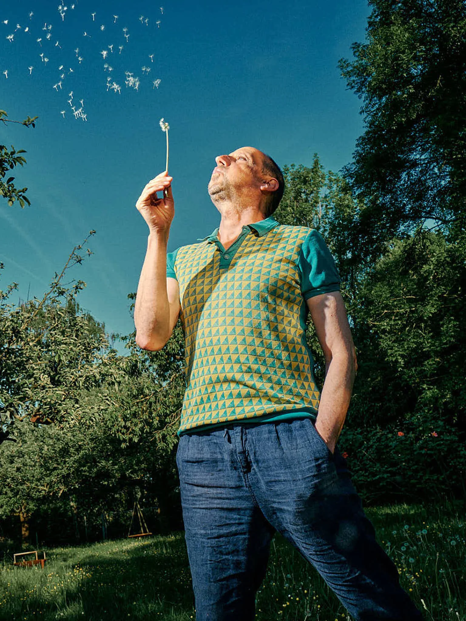 Ein Mann steht vor einem Sonnenschirm im Freien, umgeben von Büschen und Bäumen, bei sonnigem Wetter.
