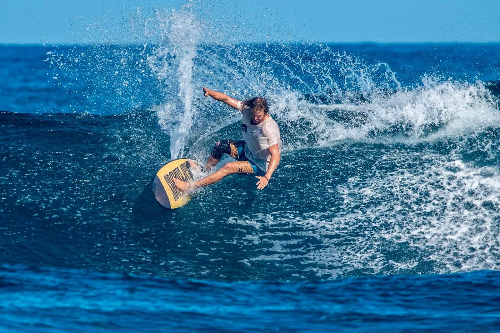 A male surfer riding a wave on a yellow surfboard in the ocean.