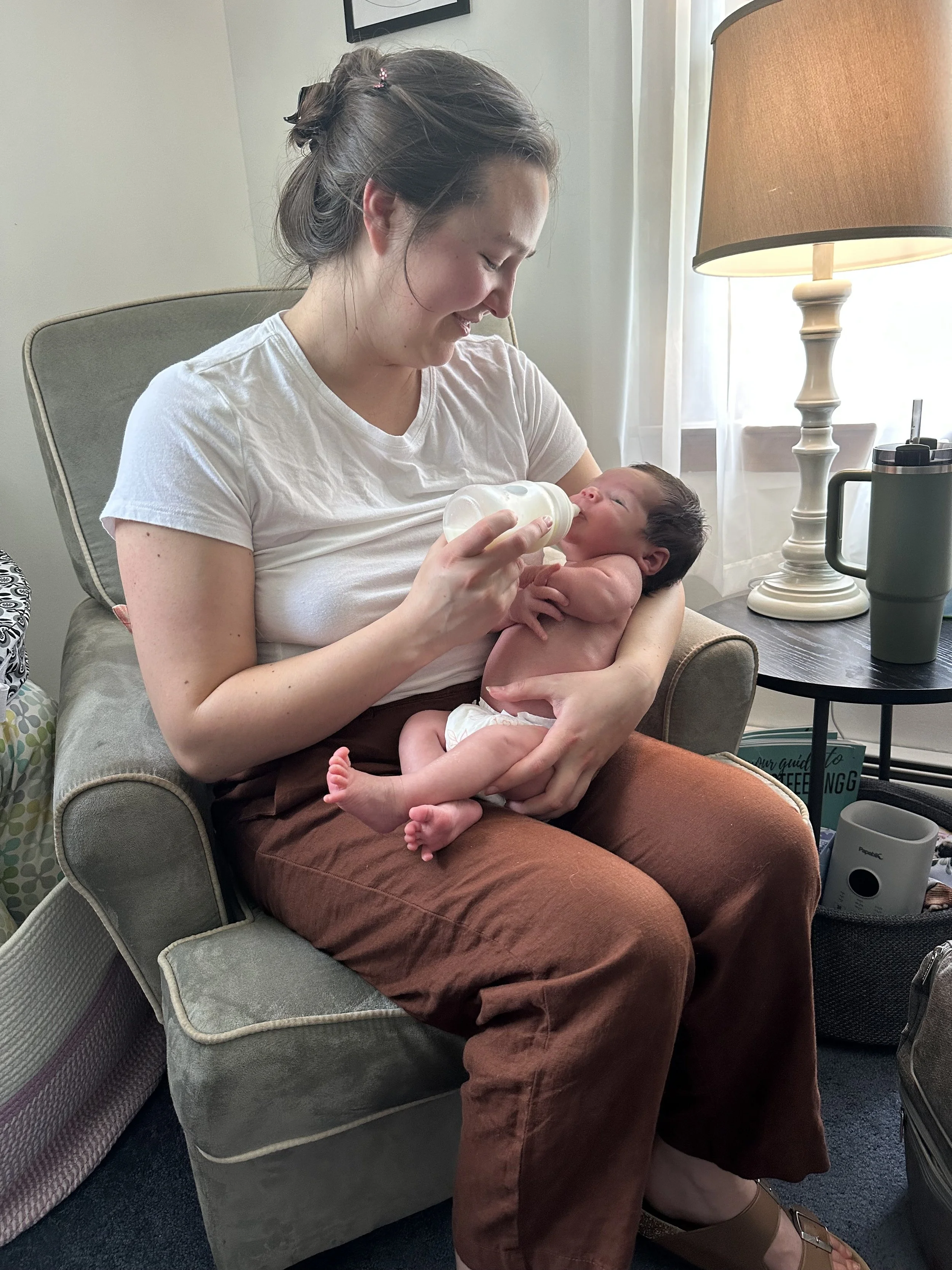 A woman feeding a newborn baby with a bottle while sitting on a chair in a cozy room.