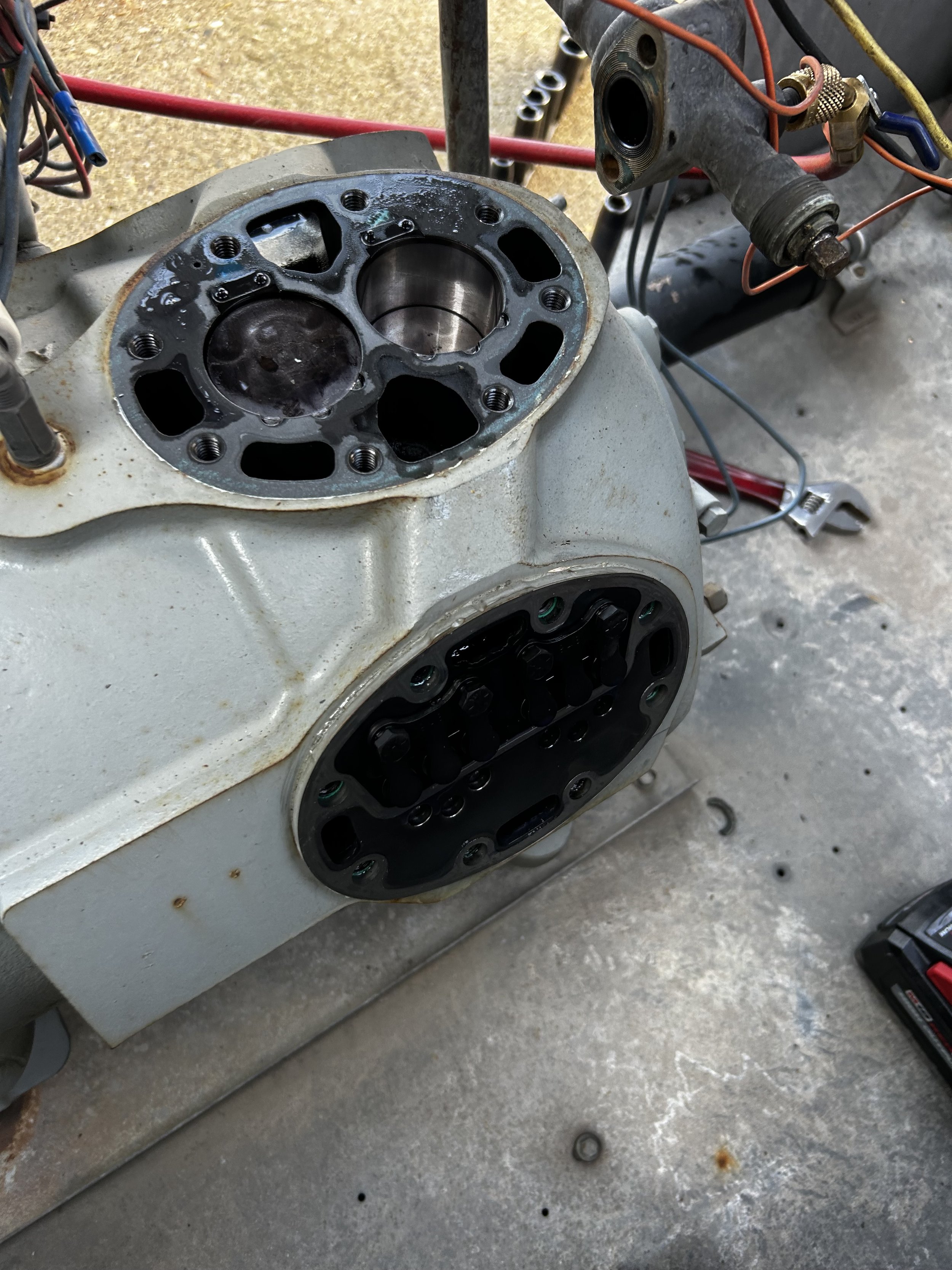 Close-up of a compesser cylinder head with the valve cover removed, showing the combustion chambers, valves, and head gasket, with various tools and wires around it.