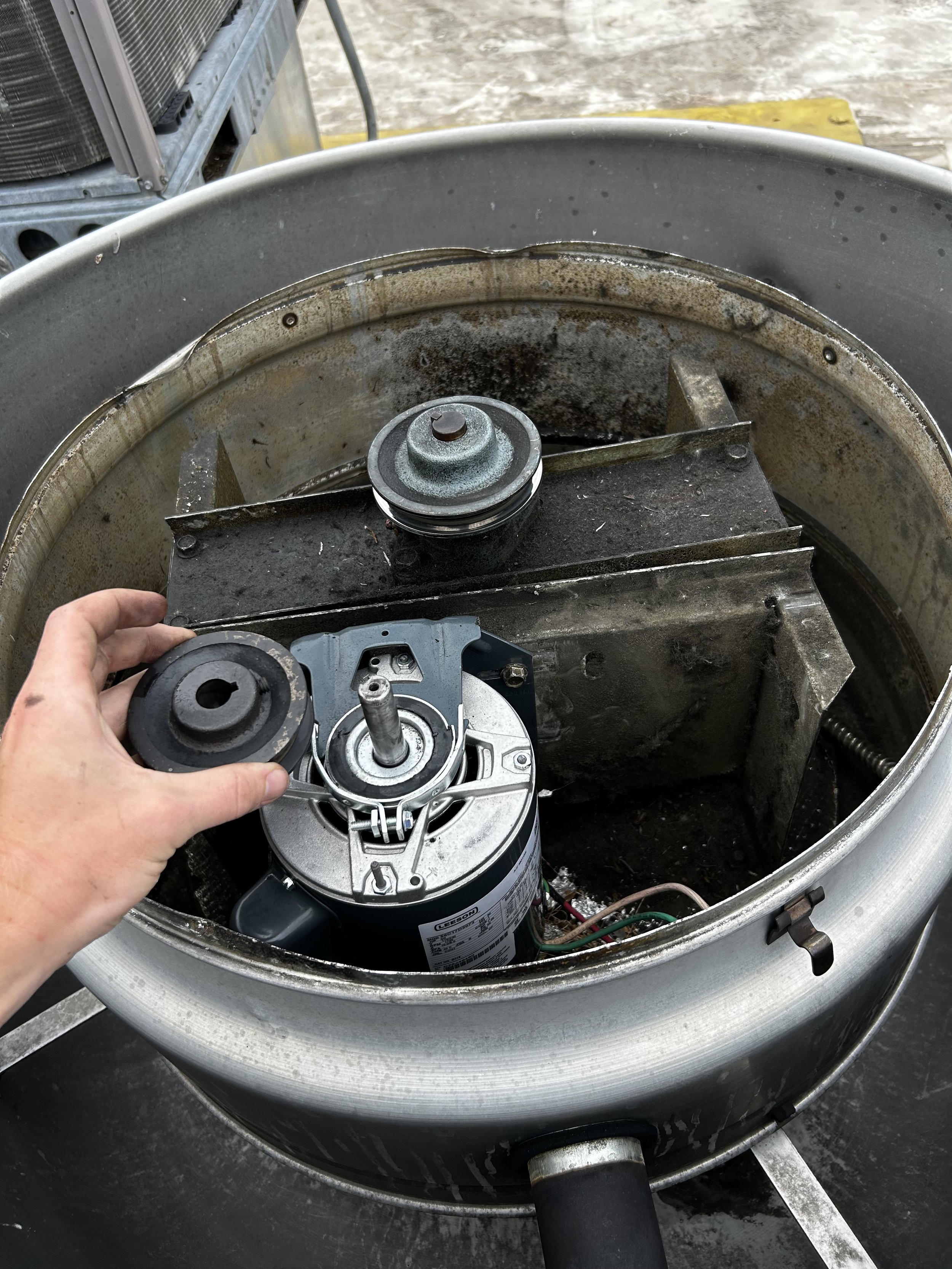 Close-up of a person removing a fan motor from a used outdoor HVAC unit, with the top cover of the unit removed revealing internal components.