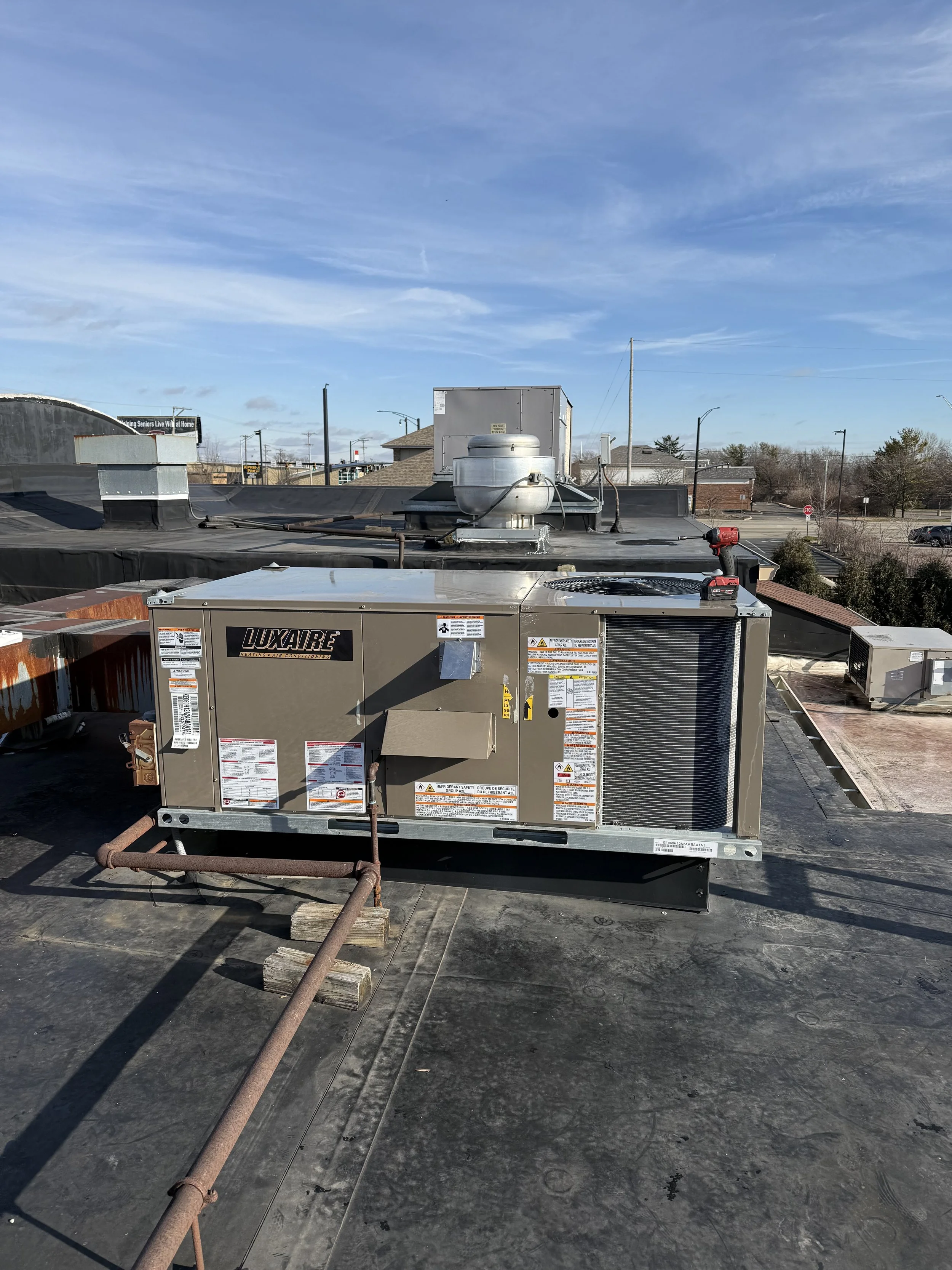 Rooftop HVAC unit with vent pipes, a red cordless drill, and a sunny sky.