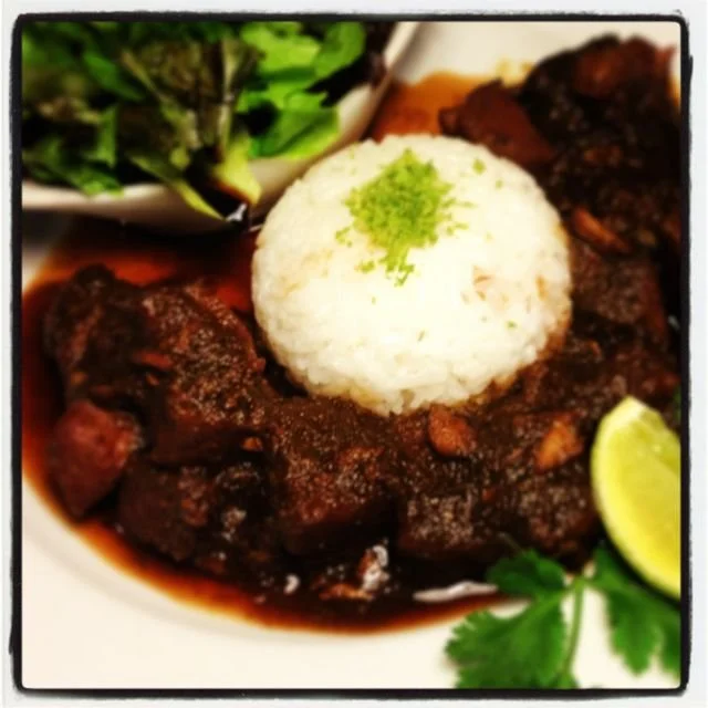 Plate of sticky ribs with white rice, garnished with lime and coriander, accompanied by salad.