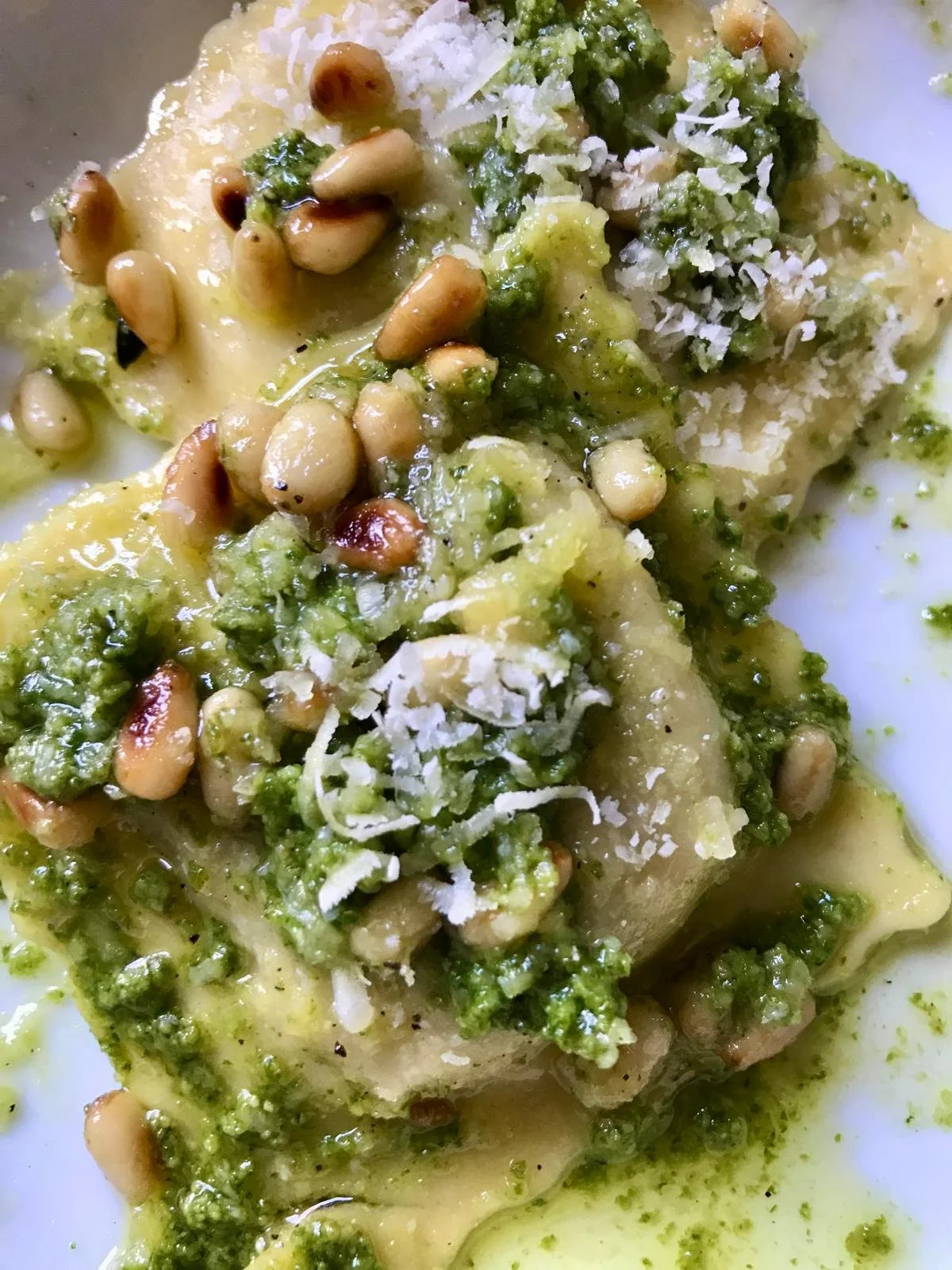 Two servings of stuffed pasta with green pesto sauce, topped with pine nuts and parmesan cheese.