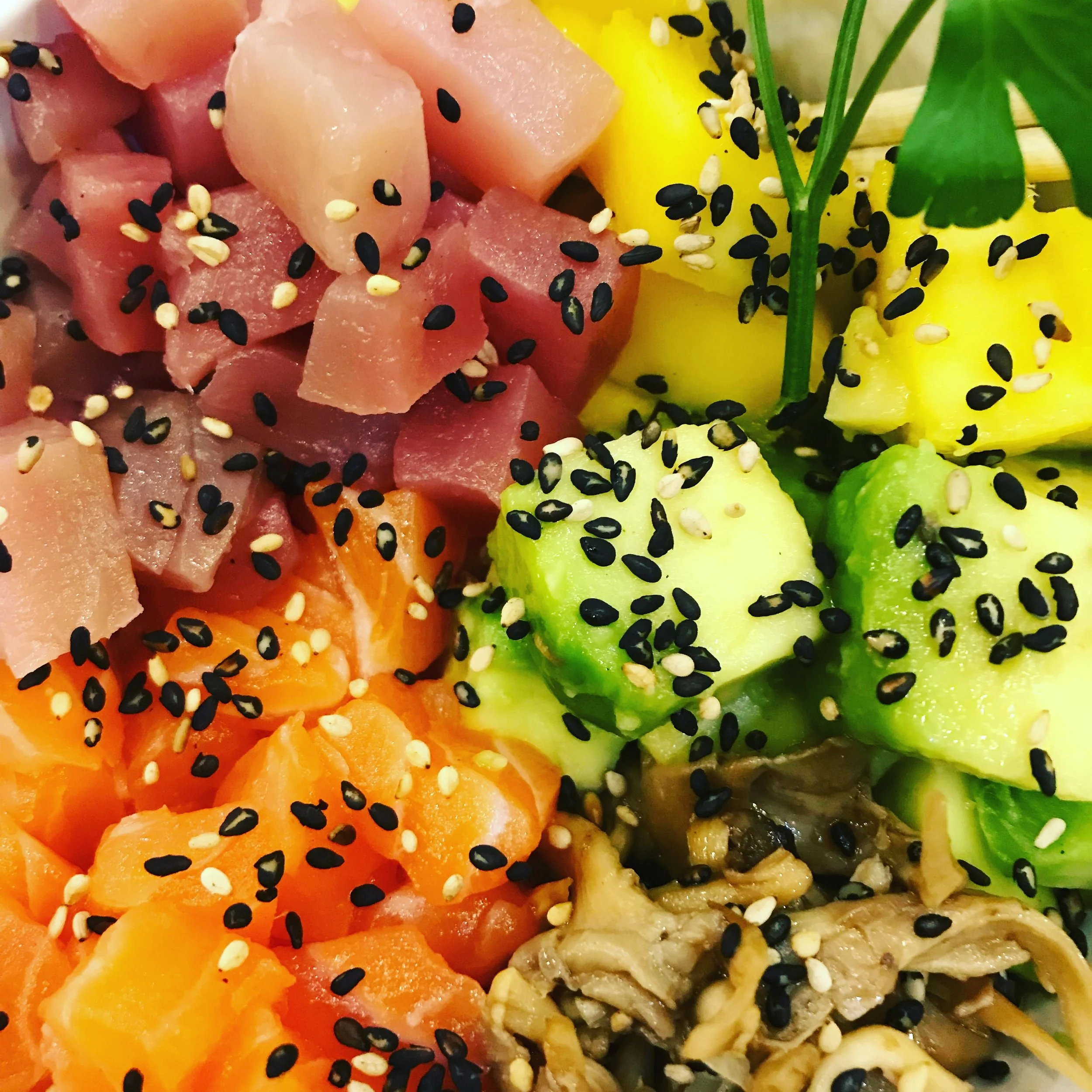 Close-up of poke bowl with diced raw fish, avocado, and vegetables, topped with black and white sesame seeds.