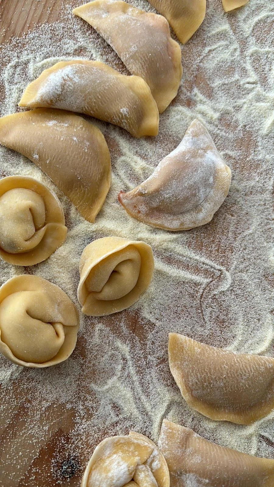 Freshly made tortellini and ravioli pasta on a floured surface.