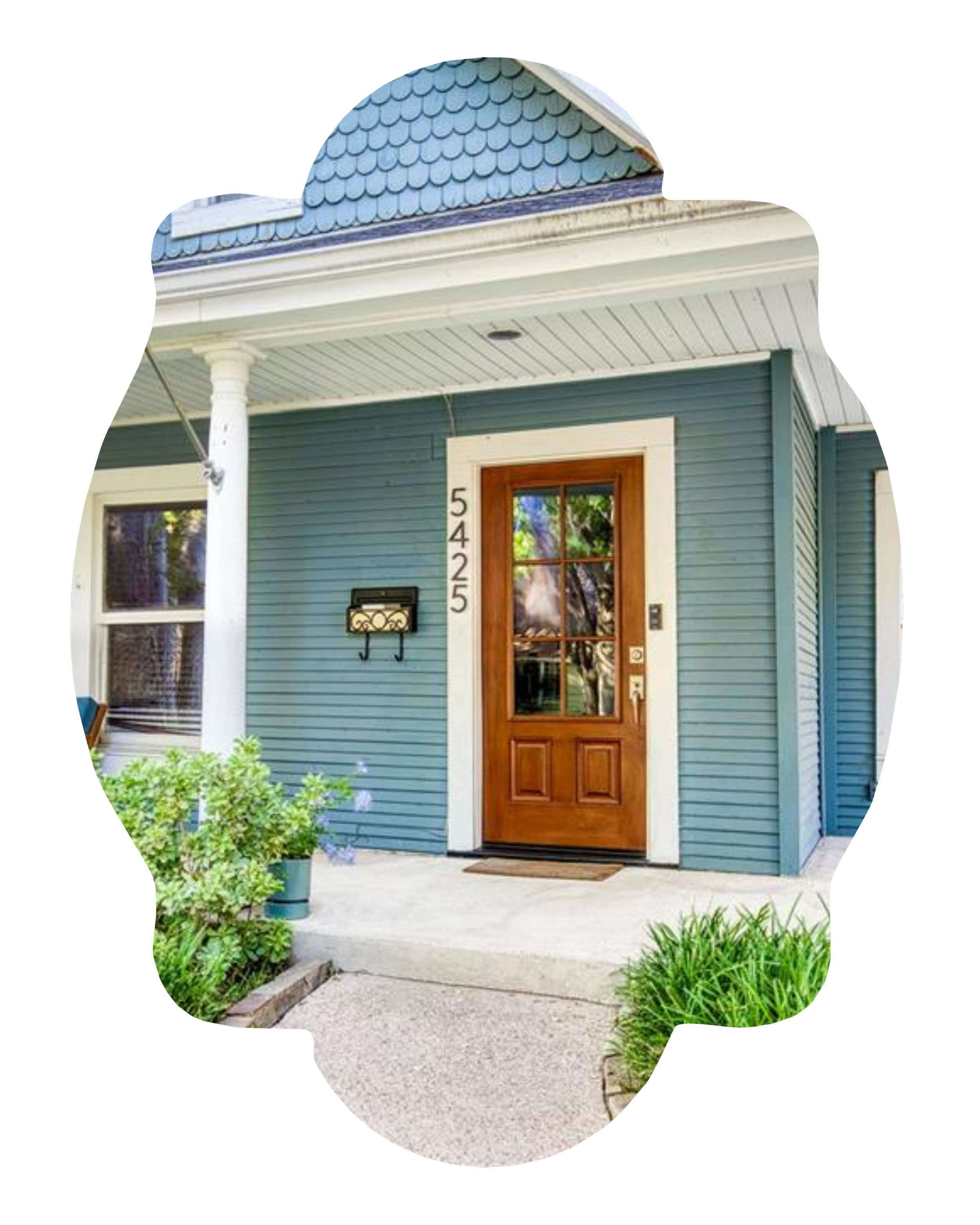 Front entrance of a house with a wooden door, blue siding, white trim, and a small garden with green plants.