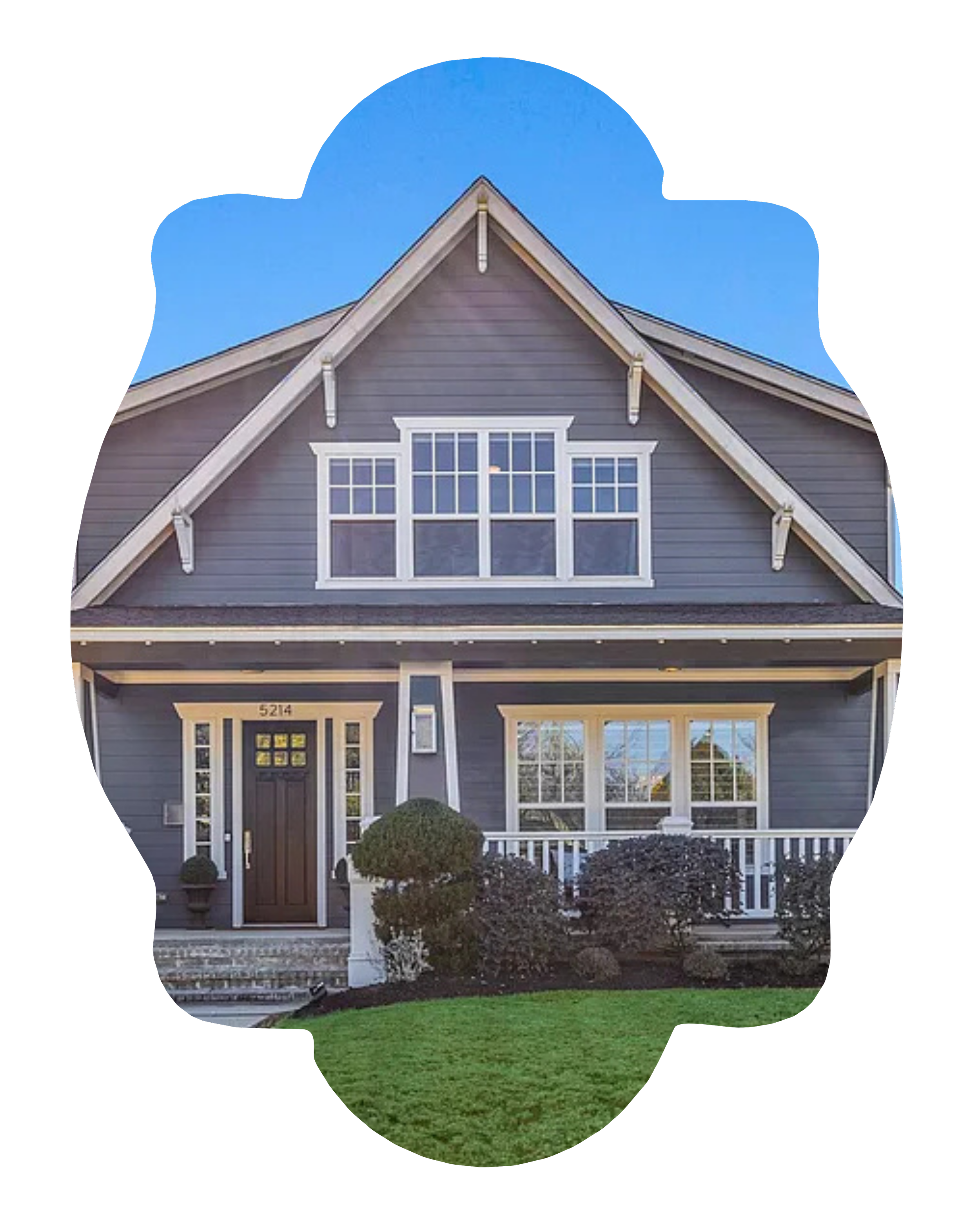 A two-story house with gray exterior, white trim, large front window, and a front porch with bushes and greenery, under a clear blue sky.