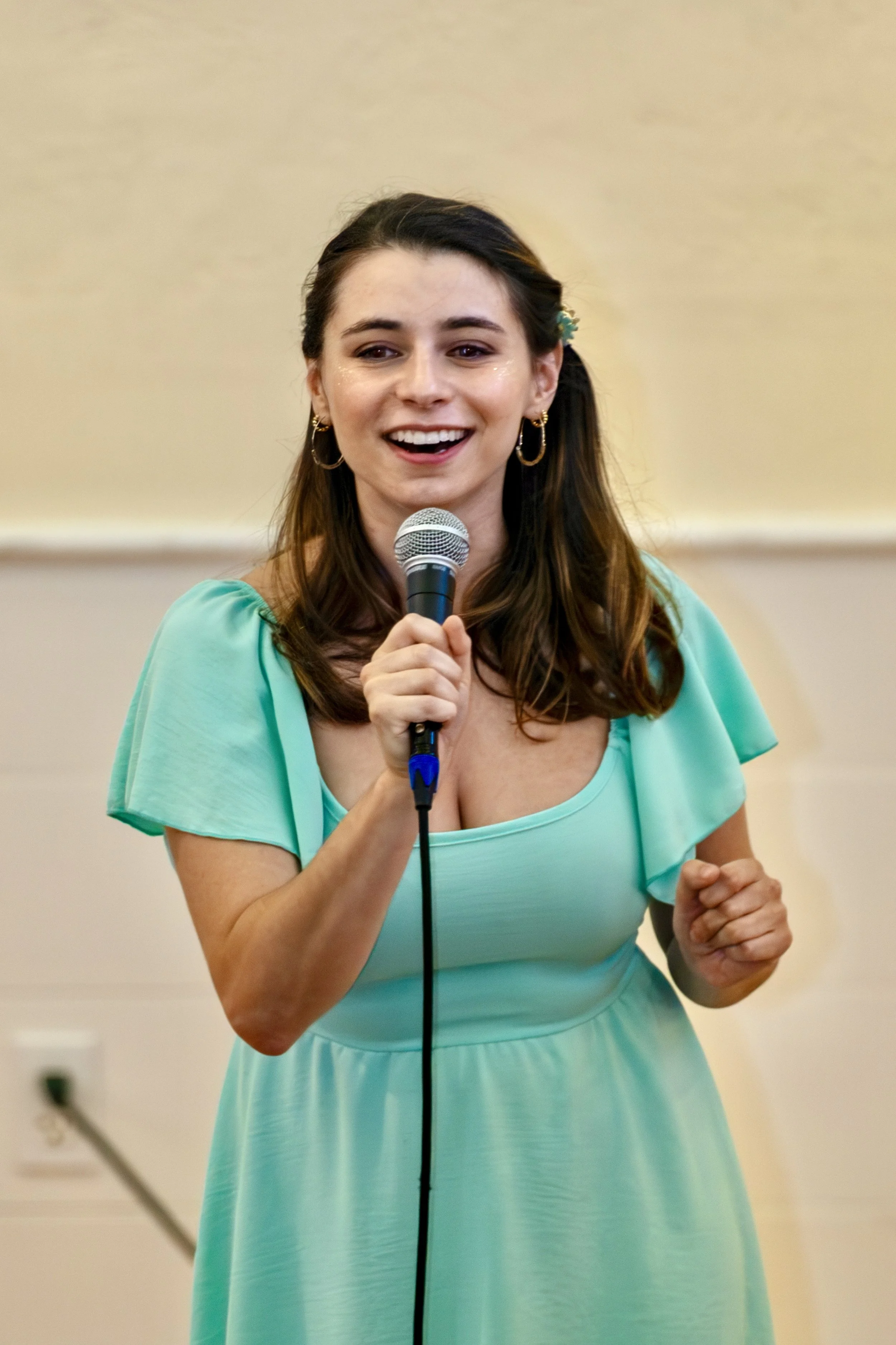 A woman in a turquoise dress holding a microphone and smiling.