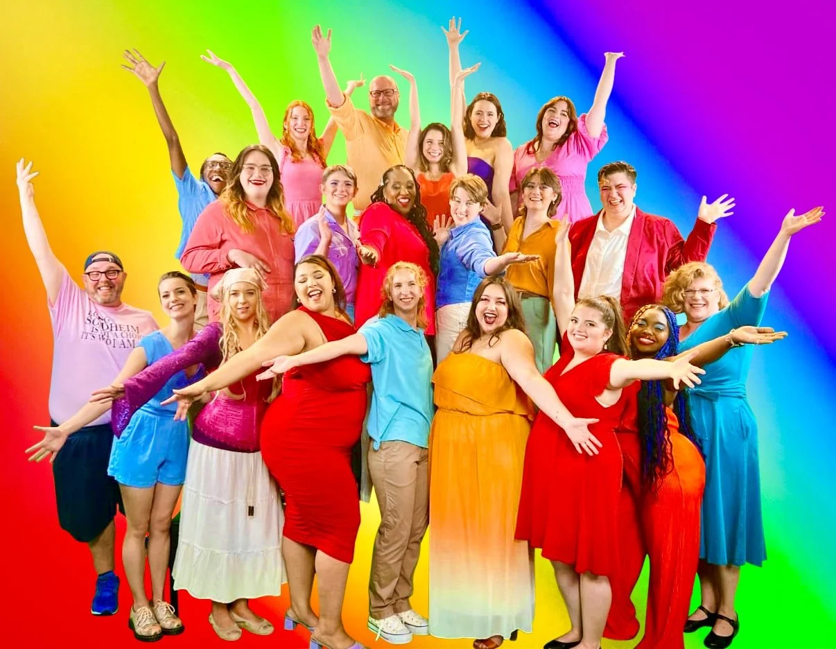 A group of diverse happy people posing with arms outstretched in front of a rainbow-colored background.