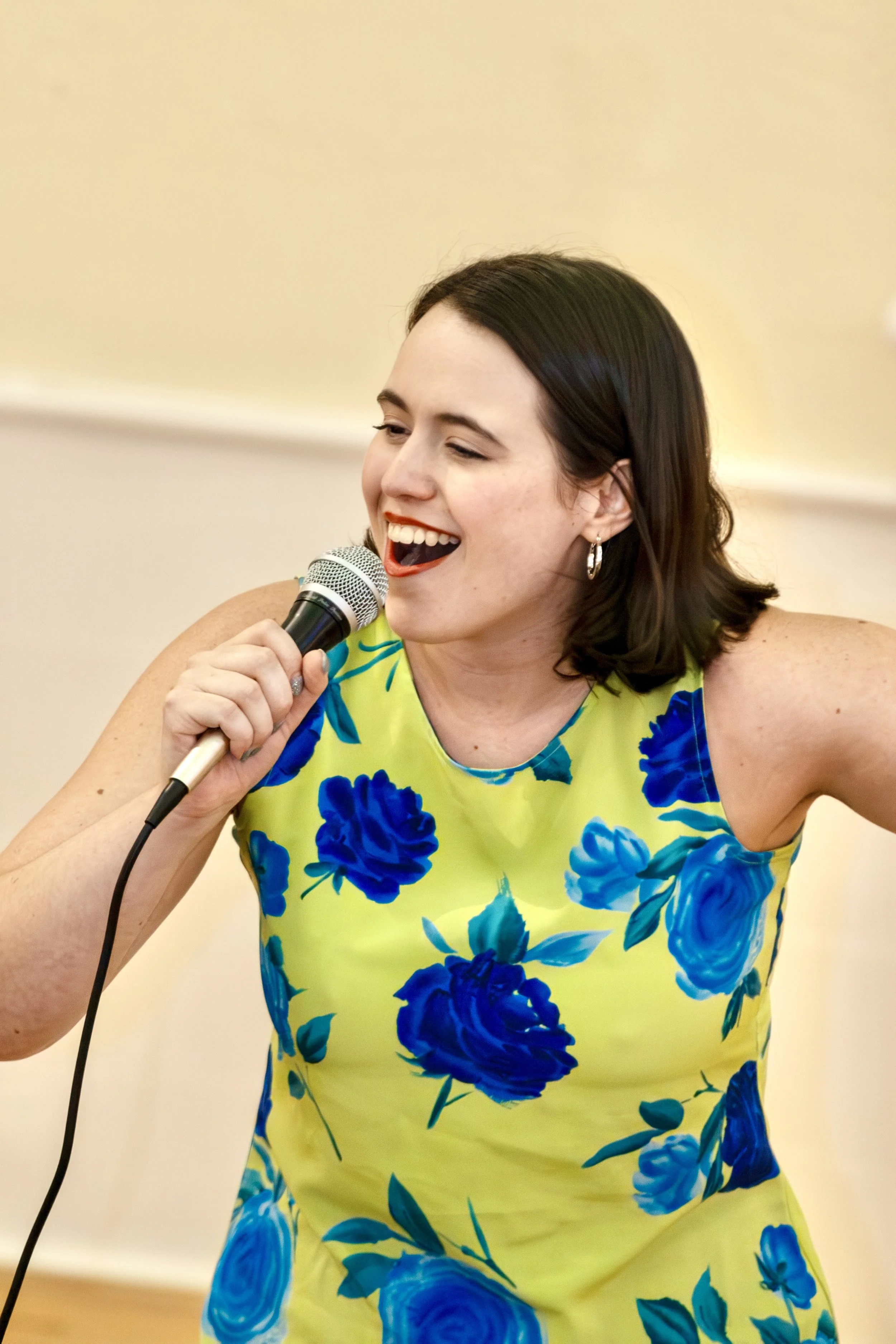 A woman singing into a microphone while wearing a sleeveless yellow dress with blue floral patterns.