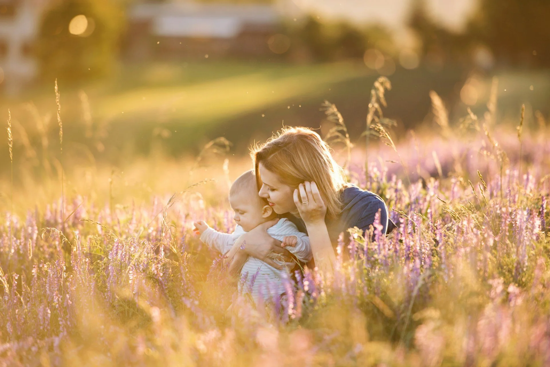 Een moeder en haar kind zitten in een veld met bloemen, omringd door geel en paars gekleurde bloemen.