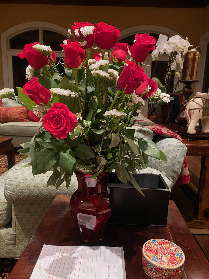 A bouquet of red roses and white flowers in a red glass vase on a wooden table.