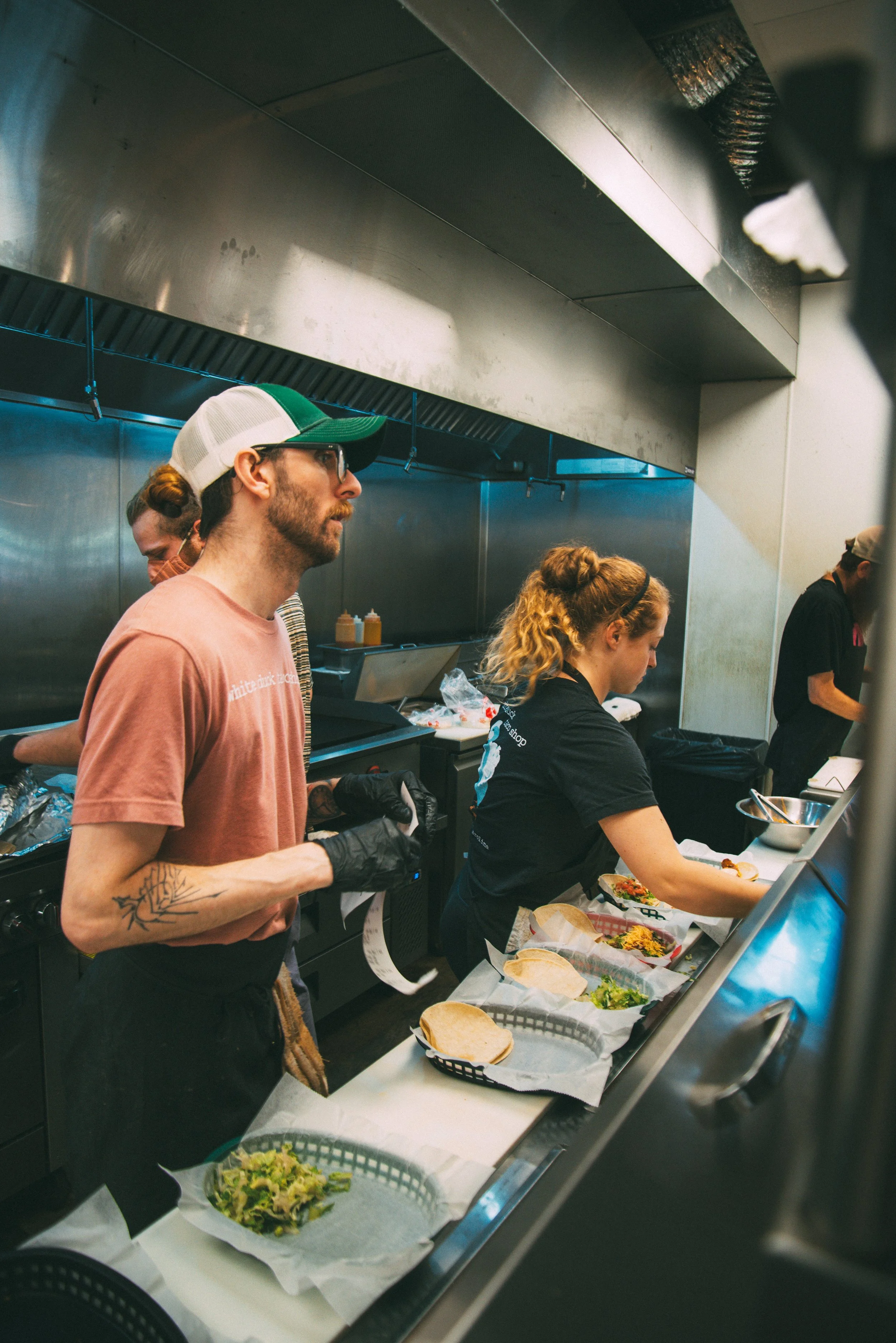 People working at a fast-food restaurant counter preparing sandwiches with various ingredients.