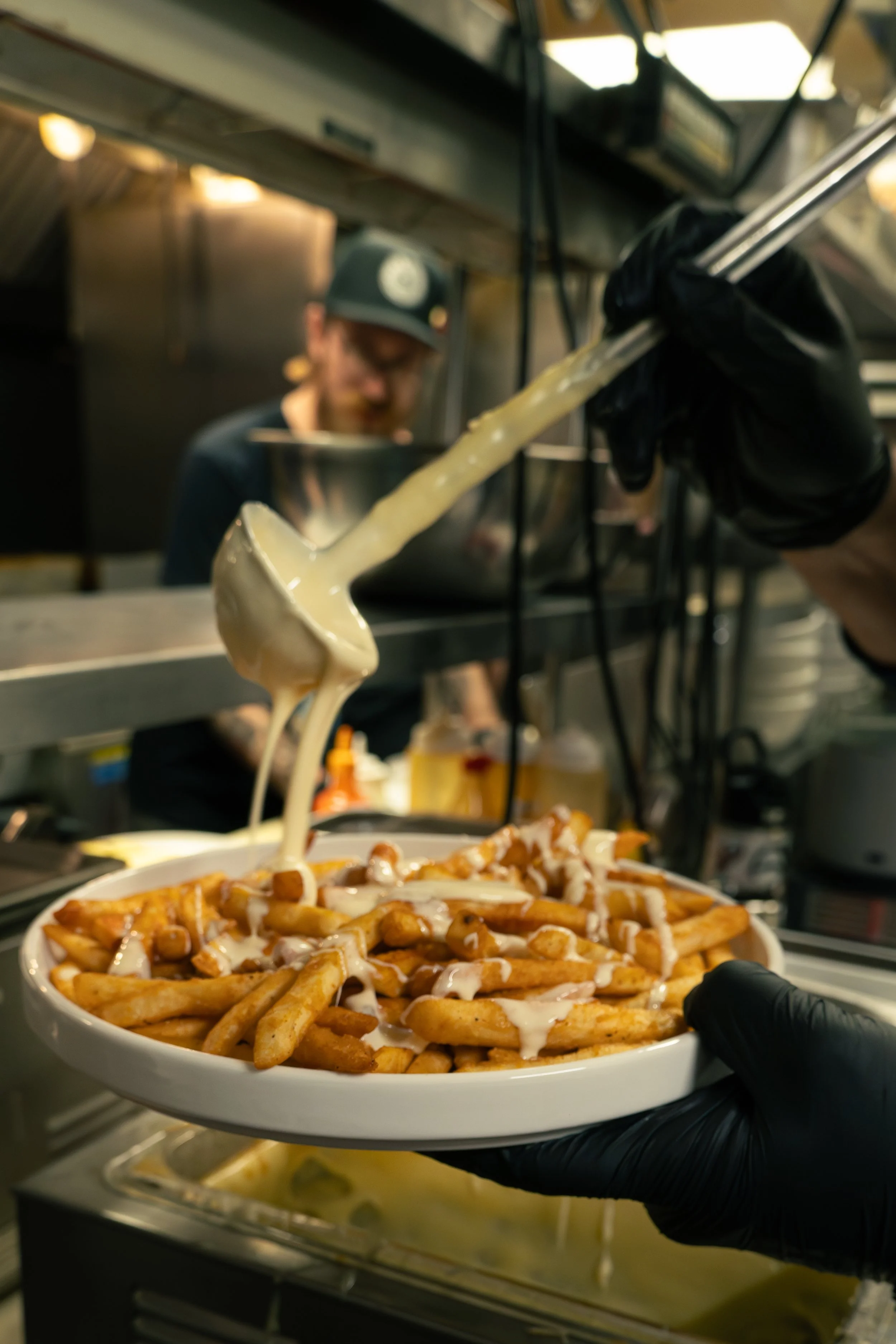 Chef preparing a plate of loaded French fries topped with cheese, gravy, and other toppings in a restaurant kitchen.