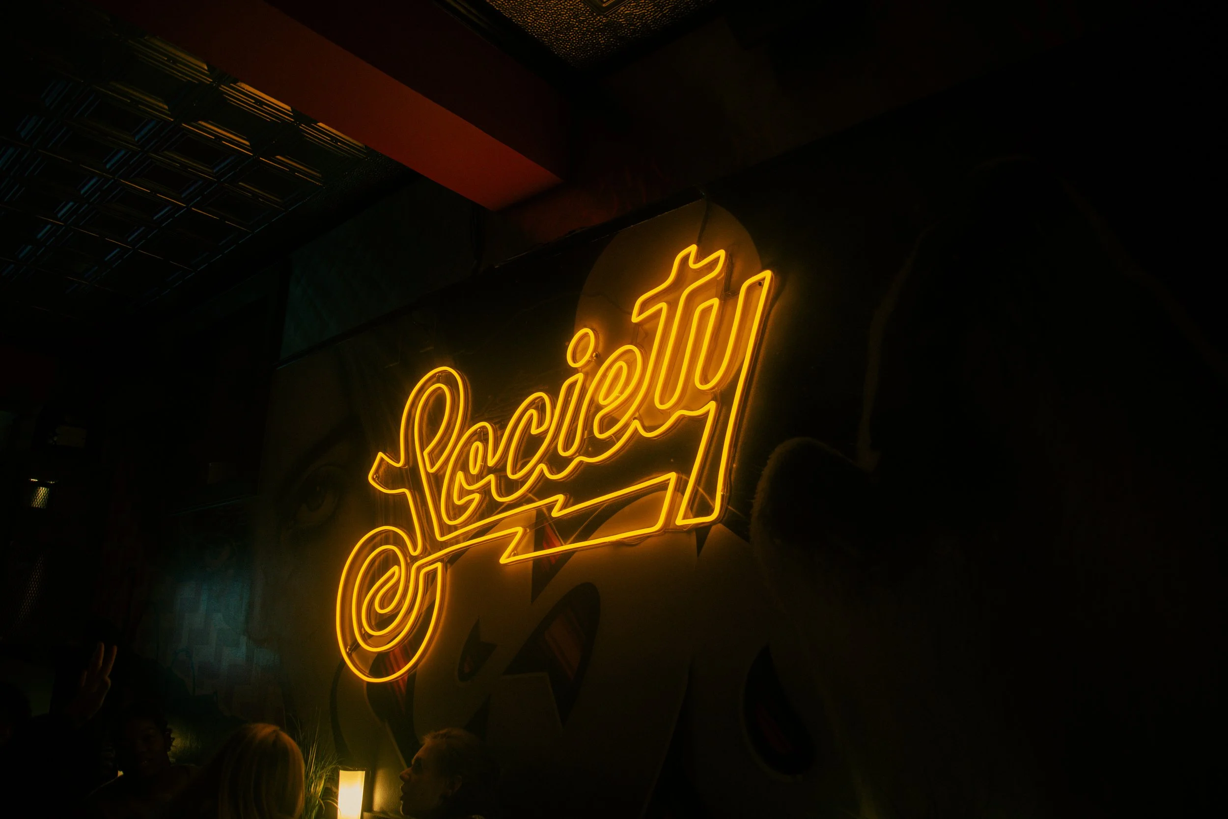 Neon sign in a dark room with the word 'Sacré' in glowing yellow letters.