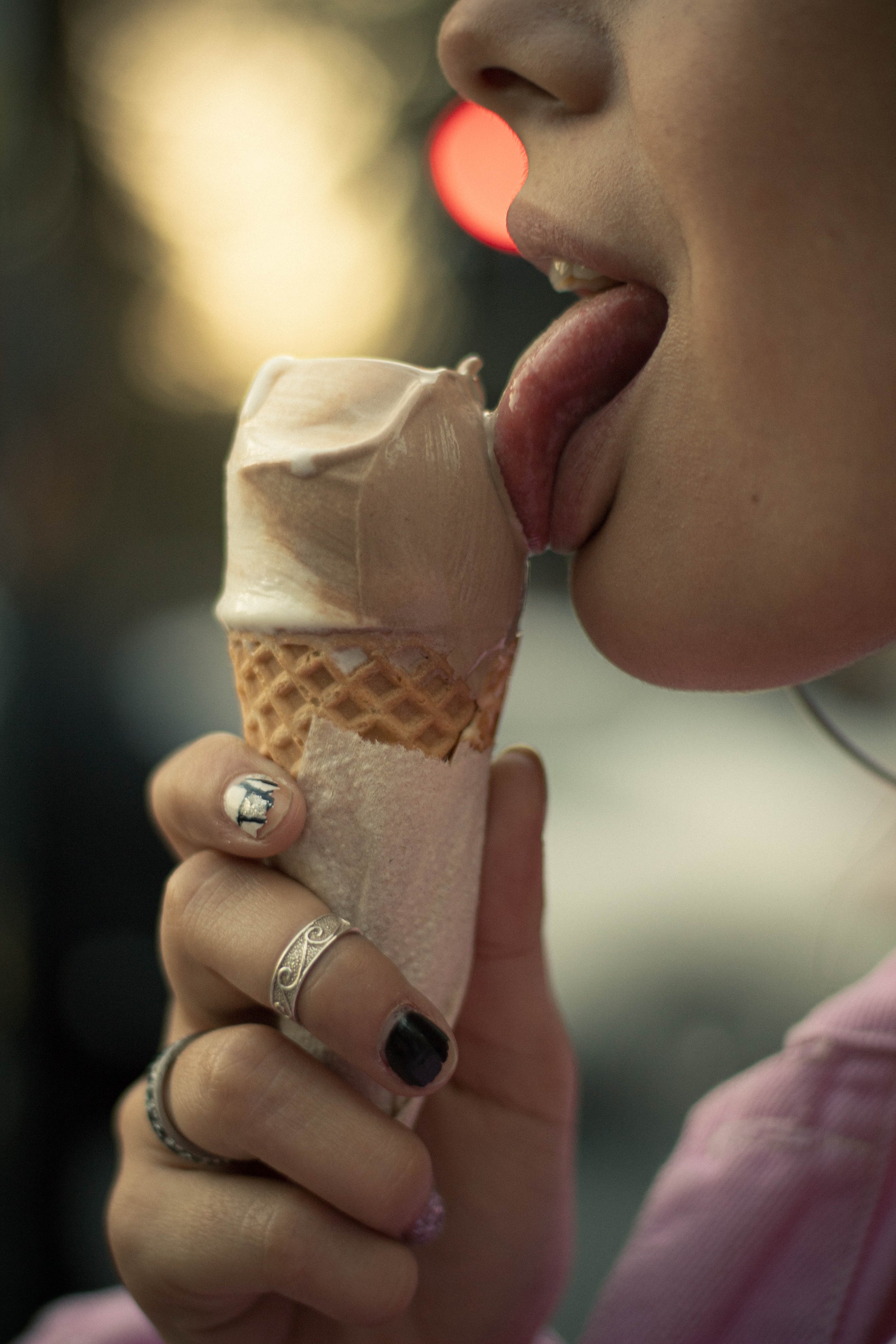 Close-up of a person holding an ice cream cone with melting vanilla ice cream, licking the ice cream with their tongue