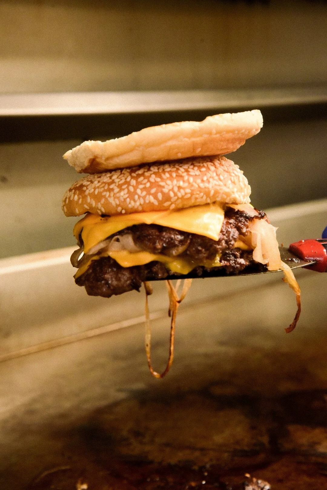 A double cheeseburger with two beef patties, melted cheese, a sesame seed bun, and a slice of ham on top.