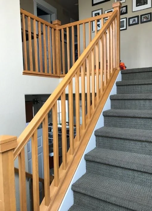 Wooden staircase with gray carpeted steps and a matching wooden handrail, leading to a loft area with framed pictures on the wall.