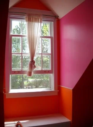 Colorful room corner with pink, orange, and brown walls, a window with sheer curtains, and greenery outside.