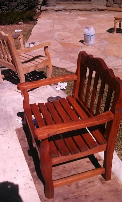 Wooden outdoor chair on a patio with other chairs and a large plastic container in the background.