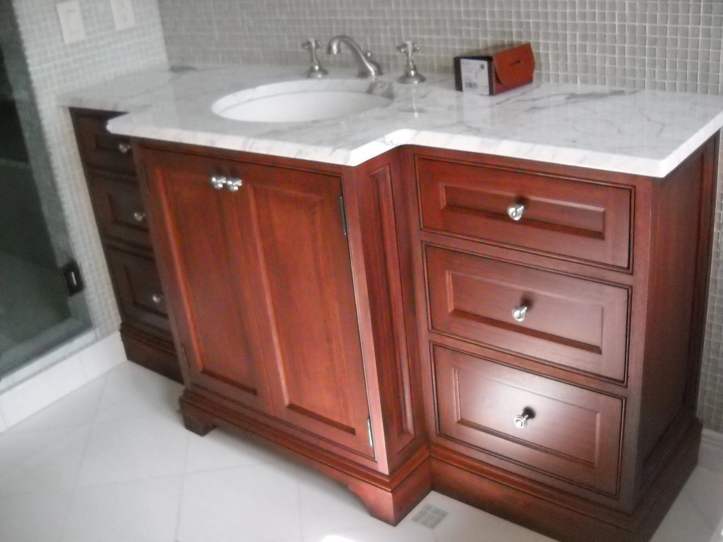Bathroom vanity with a marble countertop, a round sink, and three drawers with metallic knobs.
