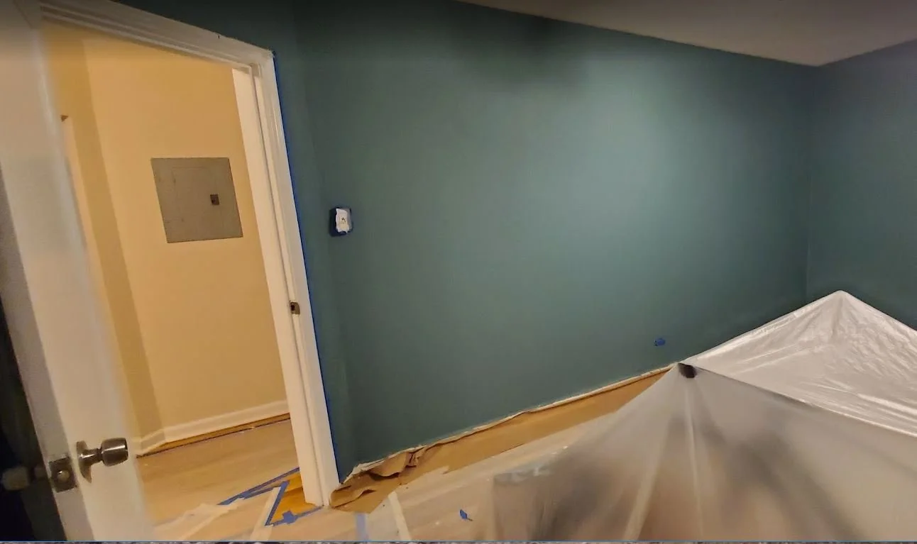 Room with painted blue wall, covered furniture, and a doorway leading to a hallway with yellow walls.
