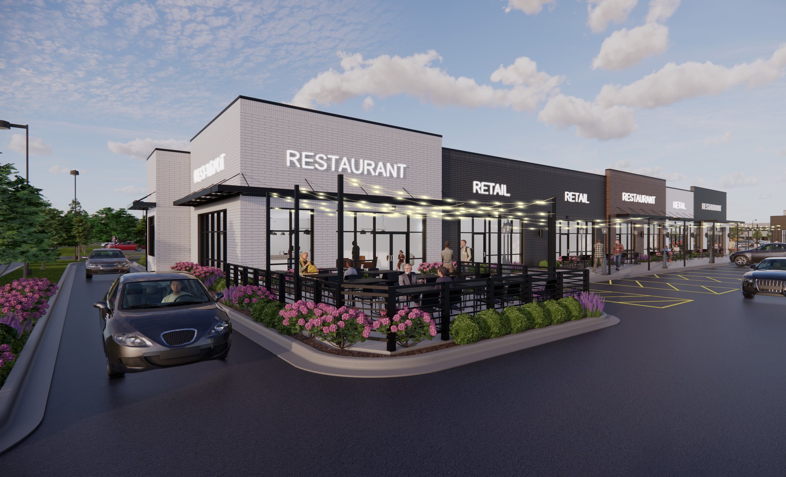 Modern retail complex with signs for restaurant and retail stores, outdoor seating area with customers, parking lot, and landscaped flower beds under a partly cloudy sky.