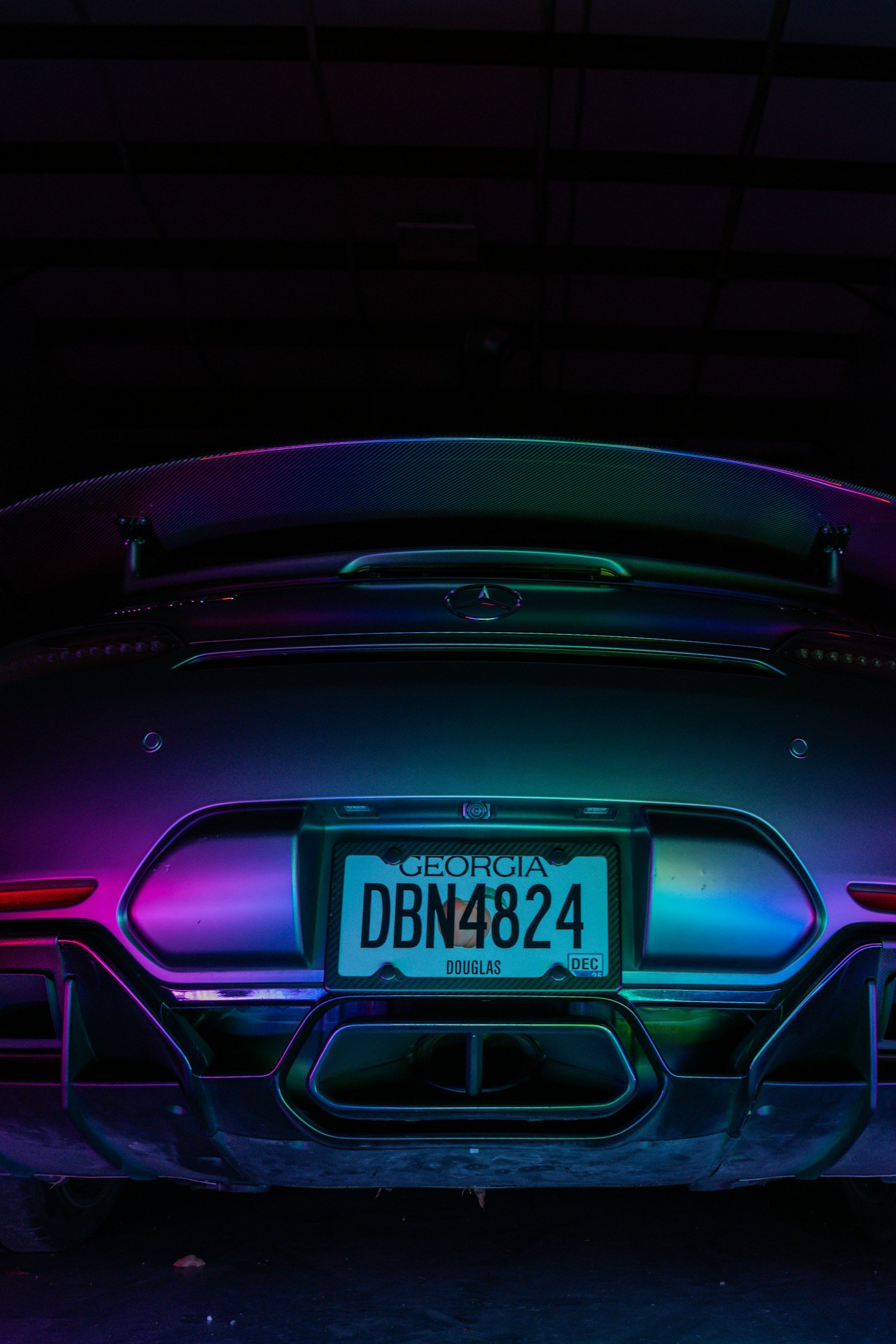 Rear view of a Mercedes-Benz car with a decorated license plate reading Georgia DBN4824, illuminated by colorful neon lights