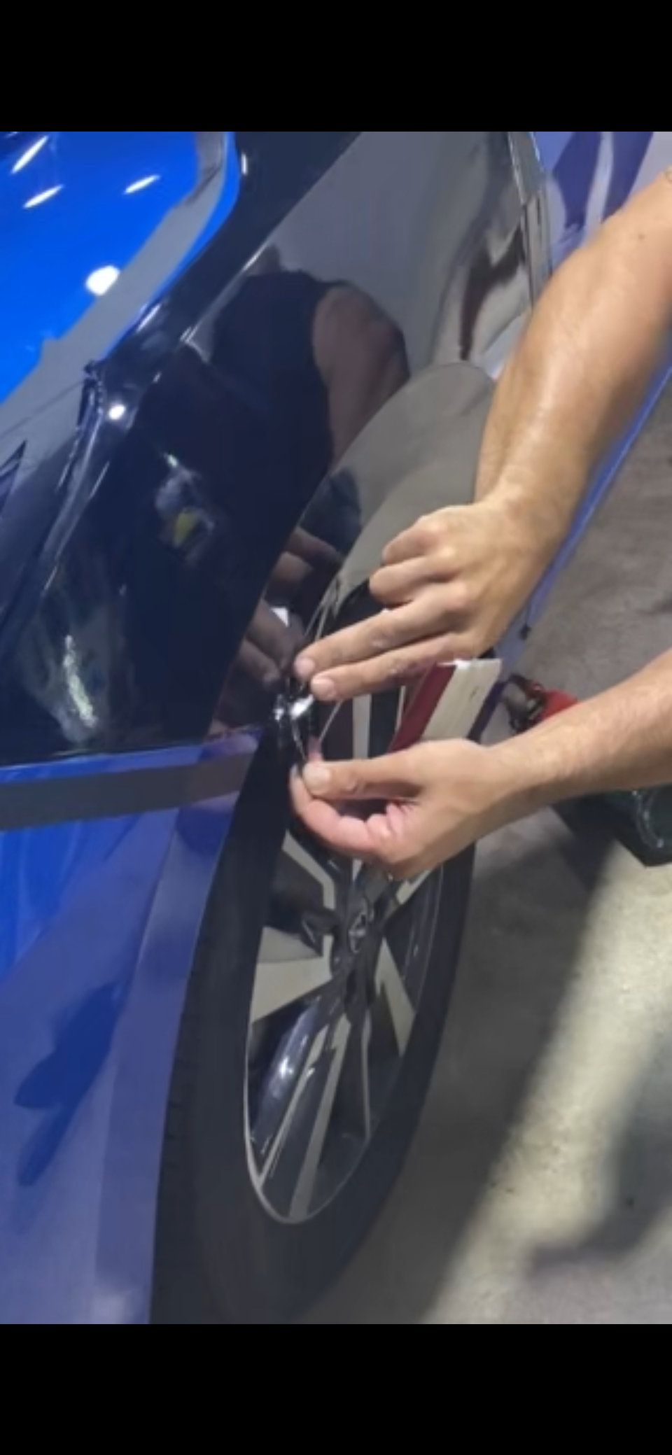 Person working on the door of a blue car, using a tool to make adjustments or repairs.