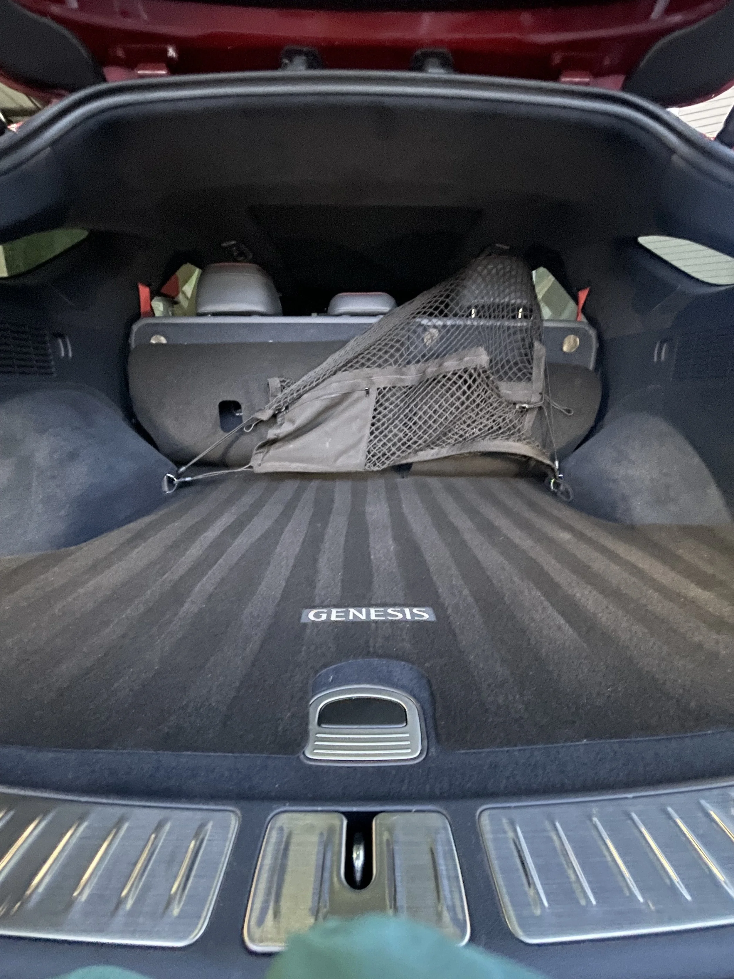 Open trunk of a red Hyundai Genesis car, showing a cargo net and two gray seats in the background.