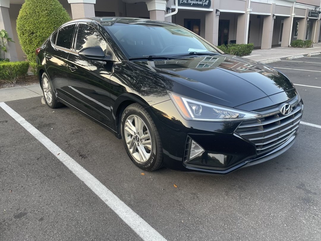 Black Hyundai sedan parked in a designated parking space in a parking lot with a building in the background.