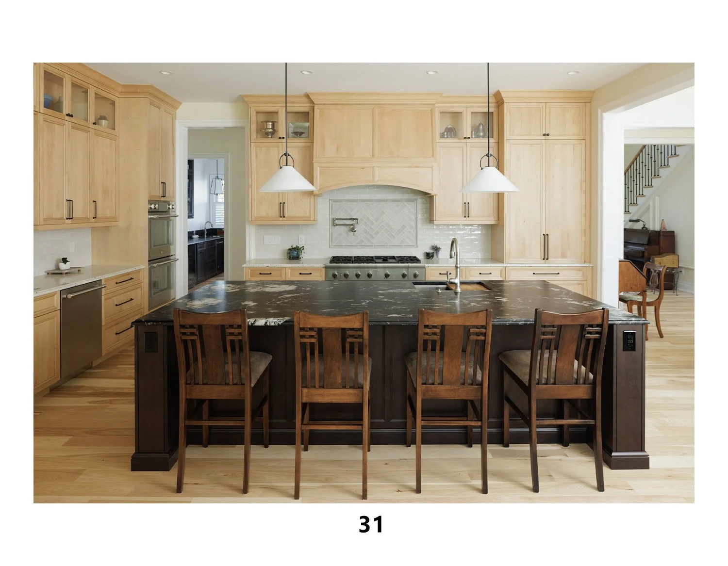 Modern kitchen with light wood cabinets, black marble island, stainless steel appliances, and pendant lights.