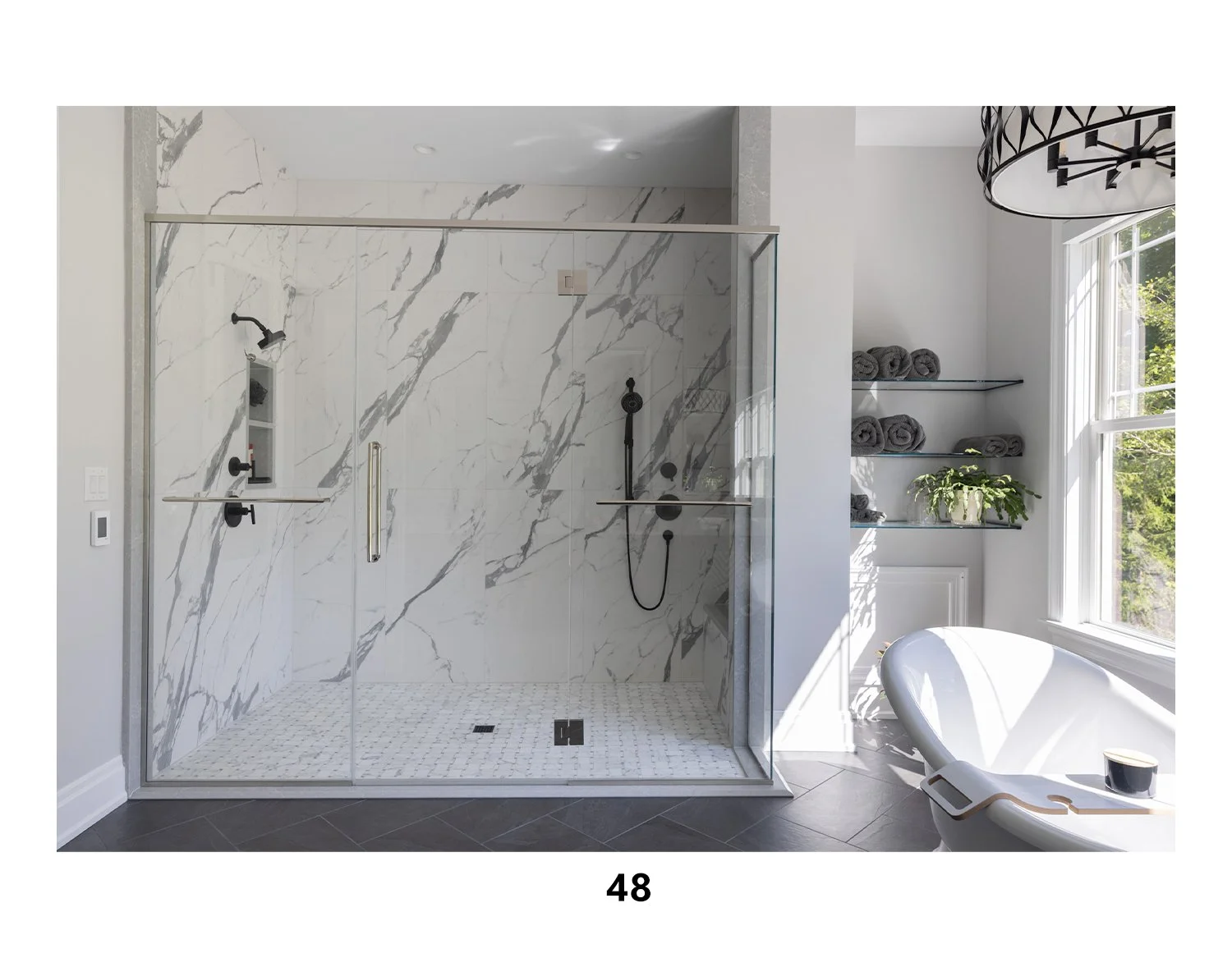 Modern bathroom with a glass-enclosed walk-in shower featuring white marble tiles with gray veining, black fixtures, and a built-in niche. To the right, there are three glass shelves holding rolled gray towels and a green potted plant. A large window