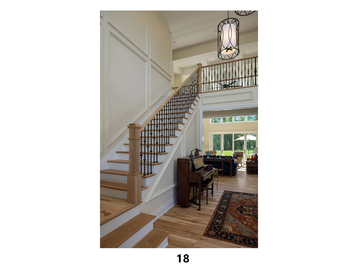 Interior view of a house with a staircase, a piano, and living area with large windows and outdoor view.