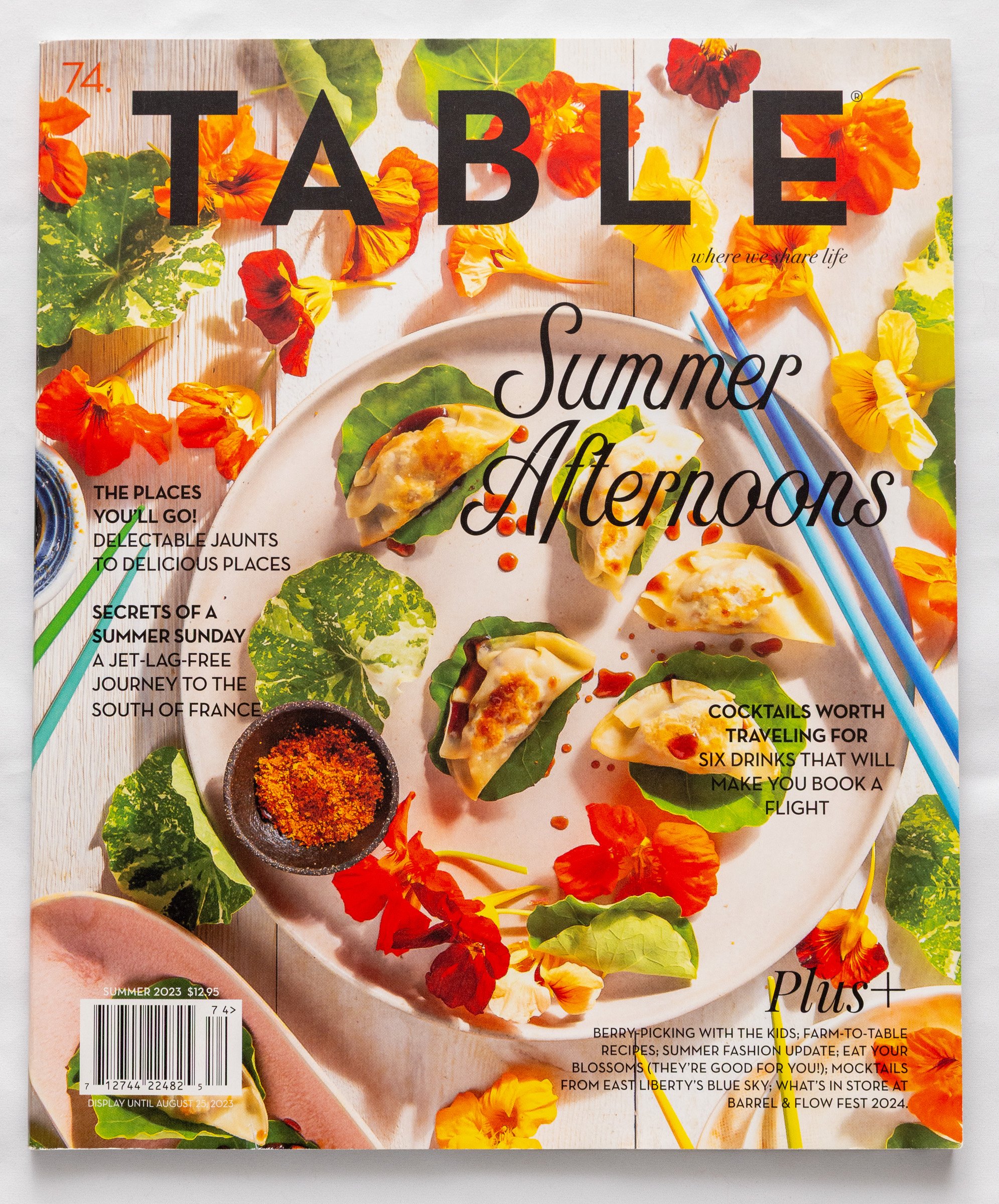 Magazine cover titled "Summer Afternoons" featuring a white plate with dumplings garnished with greens, surrounded by orange and yellow flowers, chopsticks, and a small dish of spice on a wooden surface.